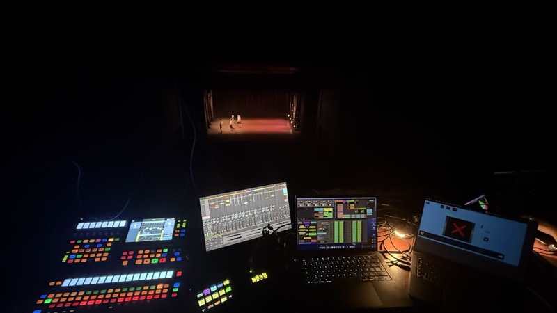 Mixing console and screens in the dark, lit stage in the distance